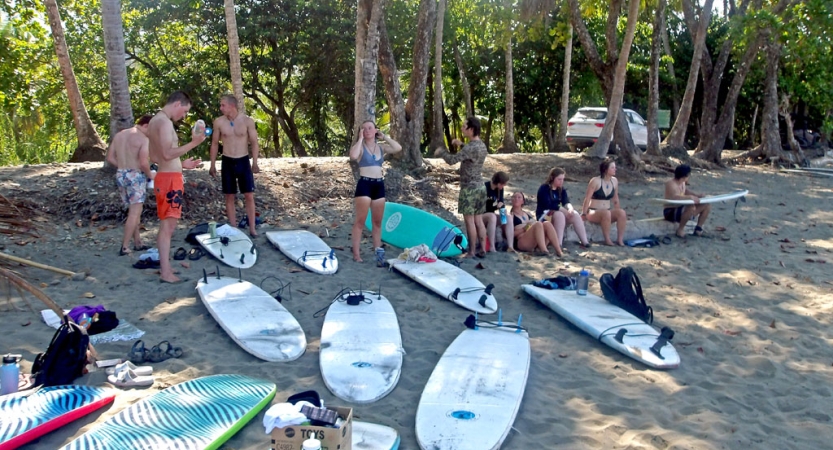 a group of people stand around several scattered surfboards on the sand